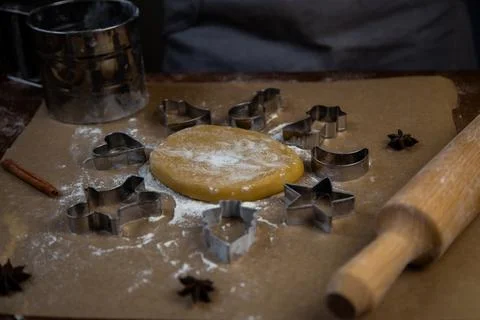 There is a dough on the parchment, around which there are cookie cutters of Stock Photos