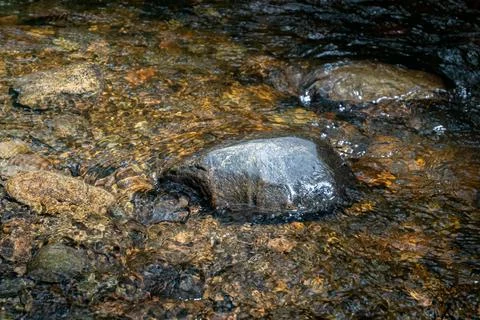 There is a large rock positioned right in the middle of a stream Stock Photos