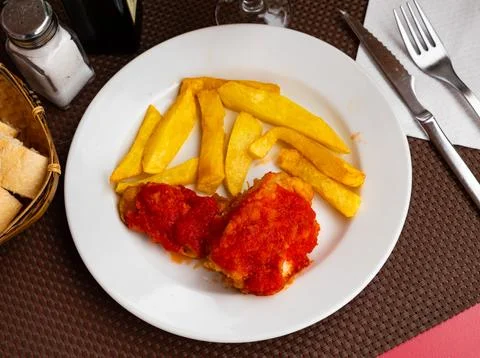 There is large slice of fried cod on plate, covered with tomato sauce and French Stock Photos