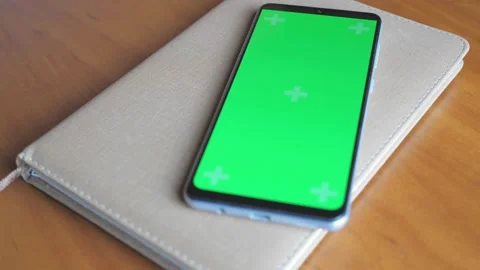 There is a notebook on a dark wooden table, on it is a phone with a green screen Stock Footage 206065547