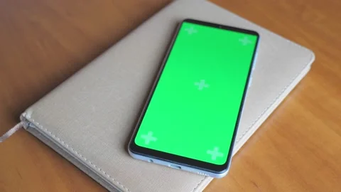 There is a notebook on a dark wooden table, on it is a phone with a green screen Stock Footage 206400537