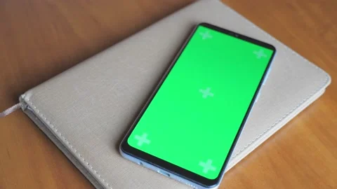 There is a notebook on a dark wooden table, on it is a phone with a green screen Stock-Footage 208660967