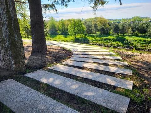 There is a path made of concrete rectangles among the trees in the park on a  Stockfoto's