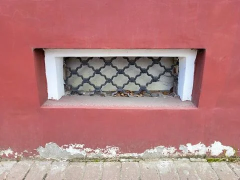 There is a small rectangular window with a wrought iron grille on the red facade Stock Photos