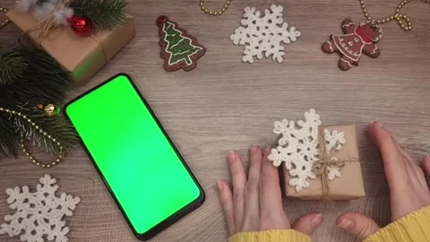 There is a smartphone with a green screen on the table, a gift and Christmas Stock Footage 315436763