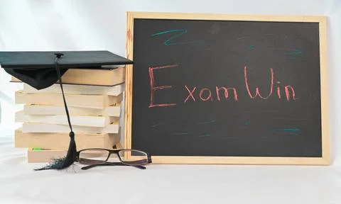 There is a stack of books placed near a blackboard that says exam win Foto stock