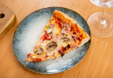 There is triangular slice of fresh pizza with bacon and mushrooms on plate. Stock Photos