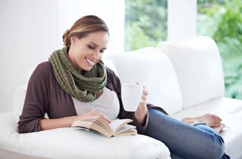Theres no enjoyment like reading. a woman resting on her sofa while reading a Stock Photos