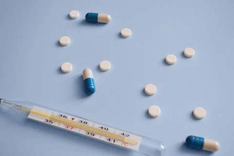 Thermometer, capsules and tablets on a blue background, medication, medical.. Stock Photos