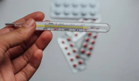 Thermometer in hand on the background of a first aid kit and pills Stock Photos