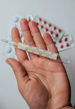Thermometer in hand on the background of a first aid kit and pills Stock Photos