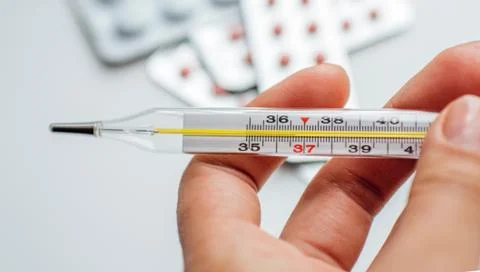 Thermometer in hand on the background of a first aid kit and pills Stock Photos