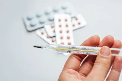 Thermometer in hand on the background of a first aid kit and pills Stock Photos