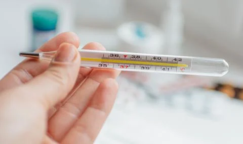 Thermometer in hand on the background of a first aid kit and pills Stock Photos