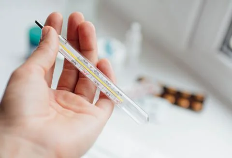 Thermometer in hand on the background of a first aid kit and pills Stock Photos