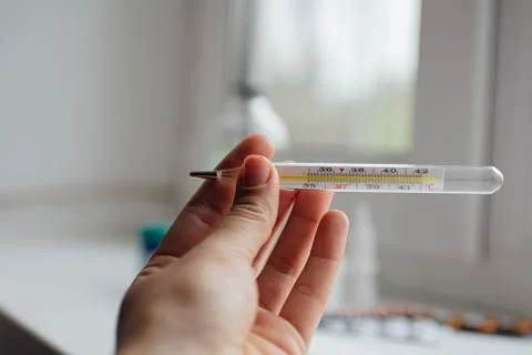 Thermometer in hand on the background of a first aid kit and pills Stock Photos