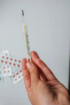 Thermometer in hand on the background of a first aid kit and pills Stock Photos