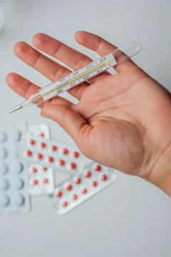 Thermometer in hand on the background of a first aid kit and pills Stock Photos