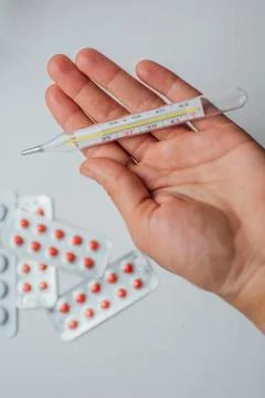 Thermometer in hand on the background of a first aid kit and pills Stock Photos