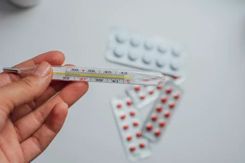 Thermometer in hand on the background of a first aid kit and pills Stock Photos