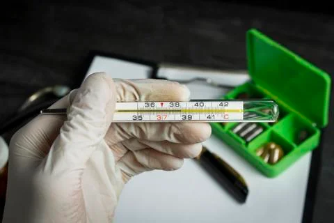 The thermometer in the hand on a background of pills Stock Photos