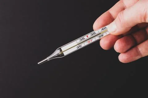 Thermometer in a hand on a black background. Stock Photos