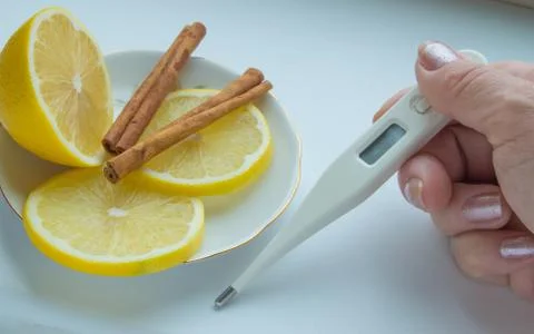 The thermometer in the hands, tablets, lemon with a cinnamon treatment Stock Photos