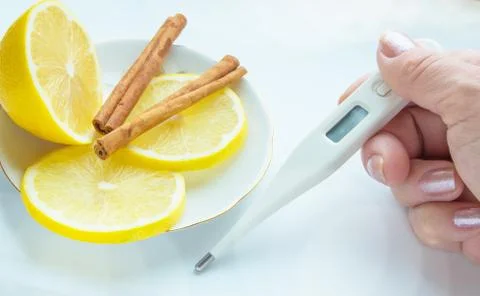 Thermometer in hands, tablets, lemon with cinnamon, the concept of treatment  Stock Photos