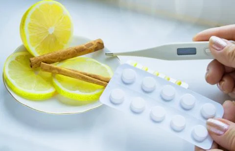 Thermometer in hands, tablets, lemon with cinnamon, the concept of treatment  Foto stock