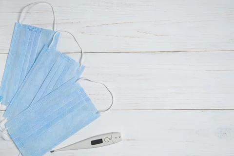 Thermometer for measuring temperature and three medical masks on white table Stock Photos