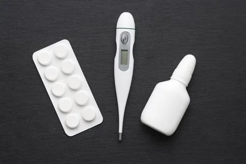 Thermometer, nasal drops and tablets on dark slate board. Flat lay. Meds for  Stock Photos