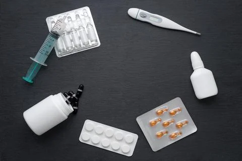 Thermometer, nasal drops tablets and ampoules with medicine on dark slate boa Stock Photos