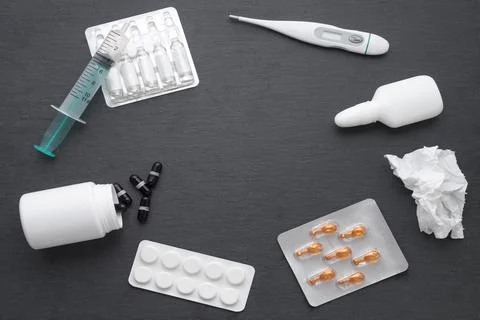 Thermometer, nasal drops tablets and ampoules with medicine on dark slate boa Stock Photos