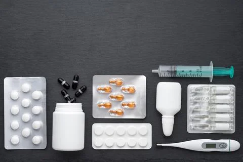 Thermometer, nasal drops tablets and ampoules with medicine on dark slate boa Stock Photos