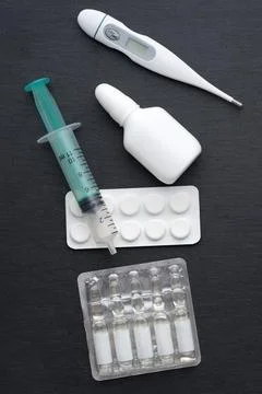 Thermometer, nasal drops tablets and ampoules with medicine on dark slate boa Stock Photos