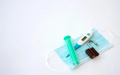 Thermometer, padlock and a syringe lying on a surgical face mask Stock Photos