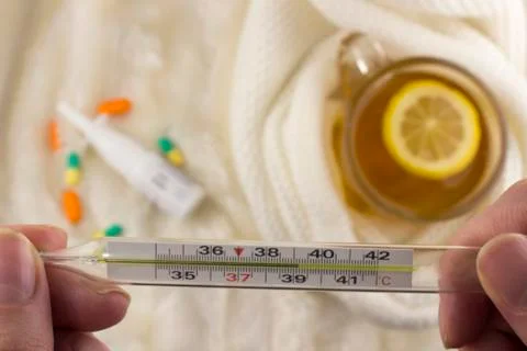 Thermometer with temperature in hands, tea with lemon Stock Photos