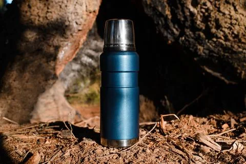 Thermos standing in a sunny forest. Vacuum travel flask close up. Stock Photos