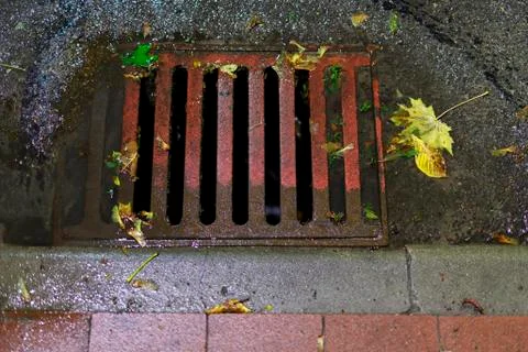Thick and solid sewer drain embedded in the road. Rainwater flowing down the  Stock Photos