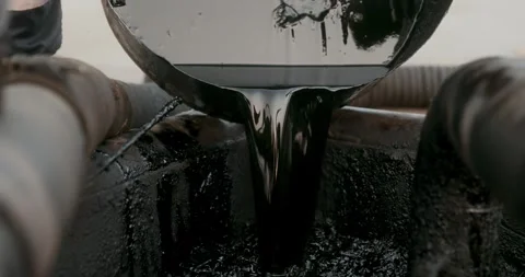 Thick black petroleum liquid pours from a metal container into an industrial 스톡 동영상 346317325