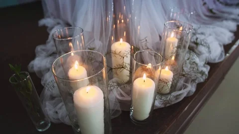Thick burning candles standing in transparent vases surrounded by textiles lit Stock Footage 97722462