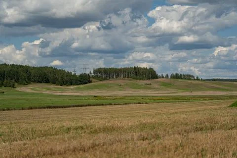 Thick clouds are flying low in the sky over green and yellow fields Stock Photos