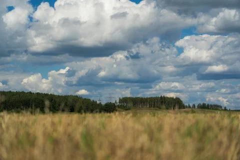 Thick clouds are flying low in the sky over green and yellow fields Stock Photos