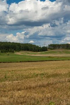 Thick clouds are flying low in the sky over green and yellow fields Stock Photos