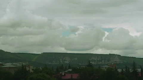 Thick clouds blanket the sky above a mountainous area. Below, trees and urban Stock Footage 312631784