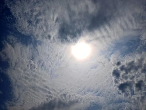 Thick clouds in the blue sky around the sun. The sun is at its zenith Stock Photos