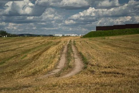 Thick clouds over a dirt road in a field. The road to the field after harvest Stock Photos