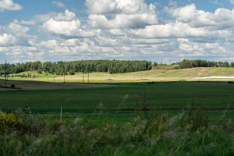 Thick clouds over green fields. The highway is far beyond the field Stock Photos