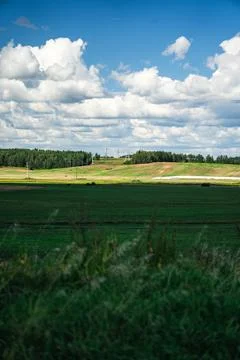 Thick clouds over green fields. The highway is far beyond the field Stock Photos