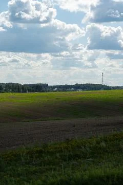 Thick clouds over green fields. The highway is far beyond the field Stock Photos